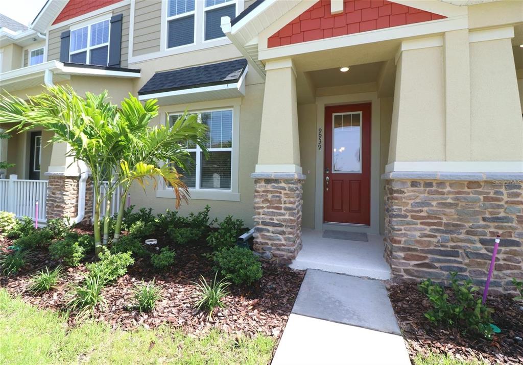 The exterior of a two-story home features a red front door, stone accents, and landscaping — 9939 RANDAL WALK STREET, ORLANDO, FL