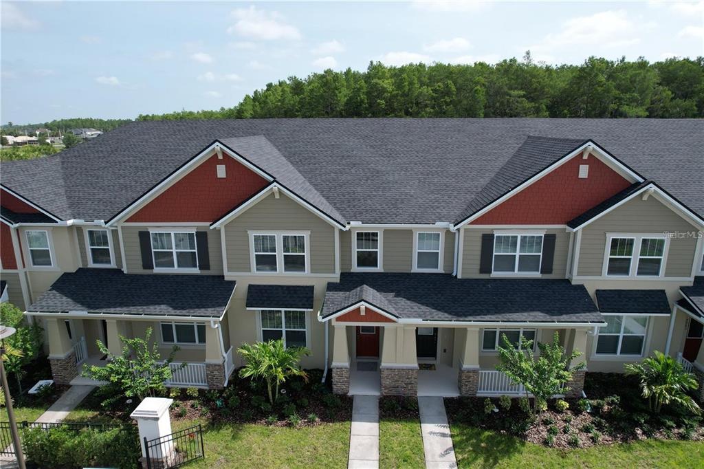 An exterior view of a multi-unit townhouse building with tan siding and red shingle accents — 9939 RANDAL WALK STREET, ORLANDO, FL