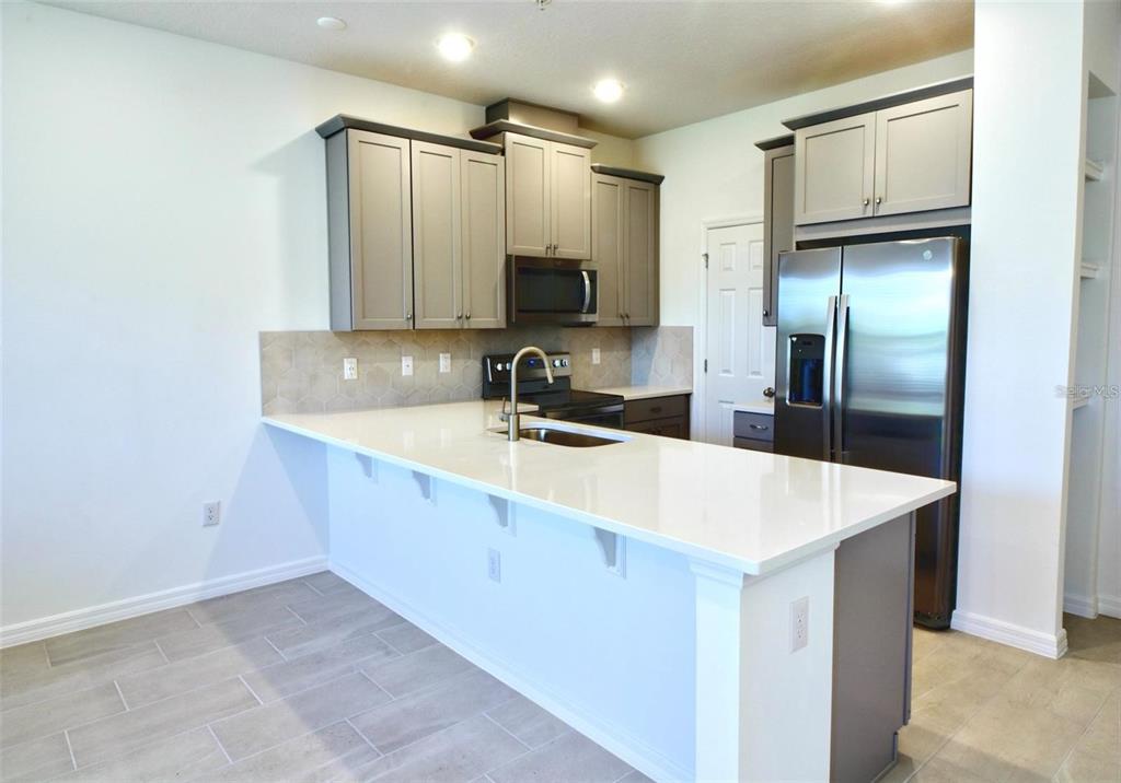 A kitchen features gray cabinets, white countertops, a stainless steel refrigerator, and tile flooring — 9939 RANDAL WALK STREET, ORLANDO, FL