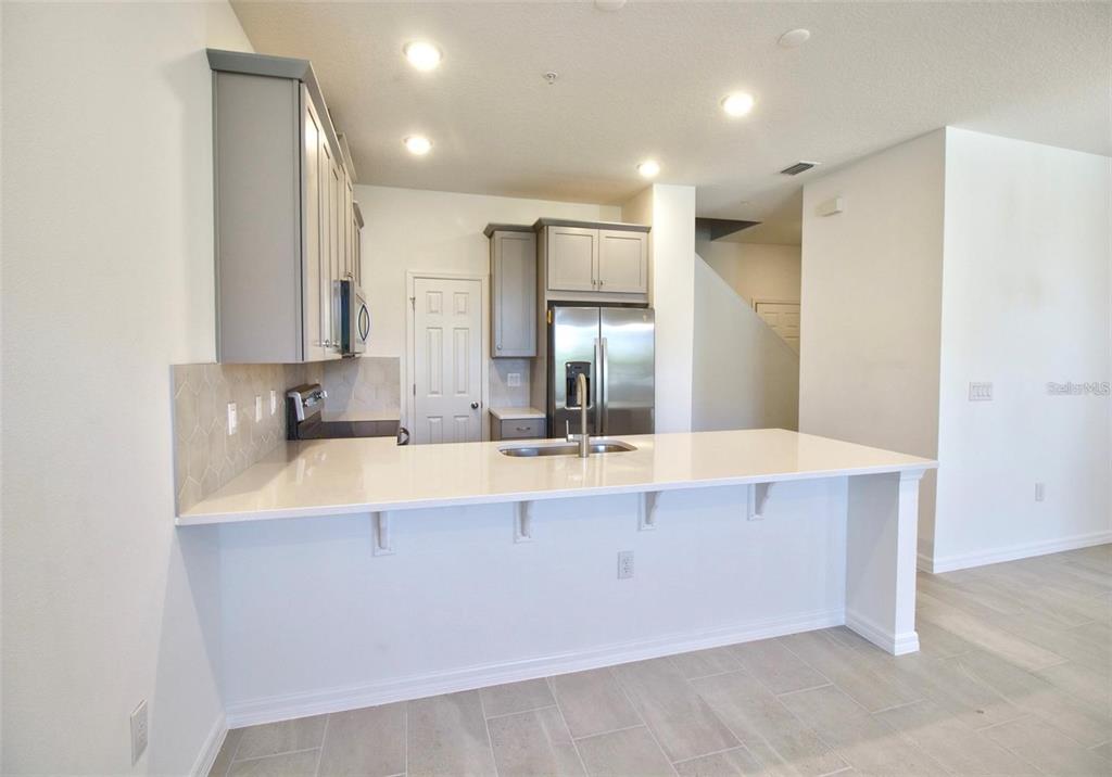A kitchen with gray cabinets, a white quartz island, and light tile flooring — 9939 RANDAL WALK STREET, ORLANDO, FL