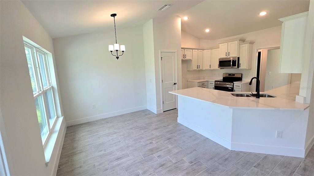 A bright kitchen and dining area features white cabinetry, quartz countertops, and light tile flooring — 2239 N BISCAYNE DRIVE, NORTH PORT, FL