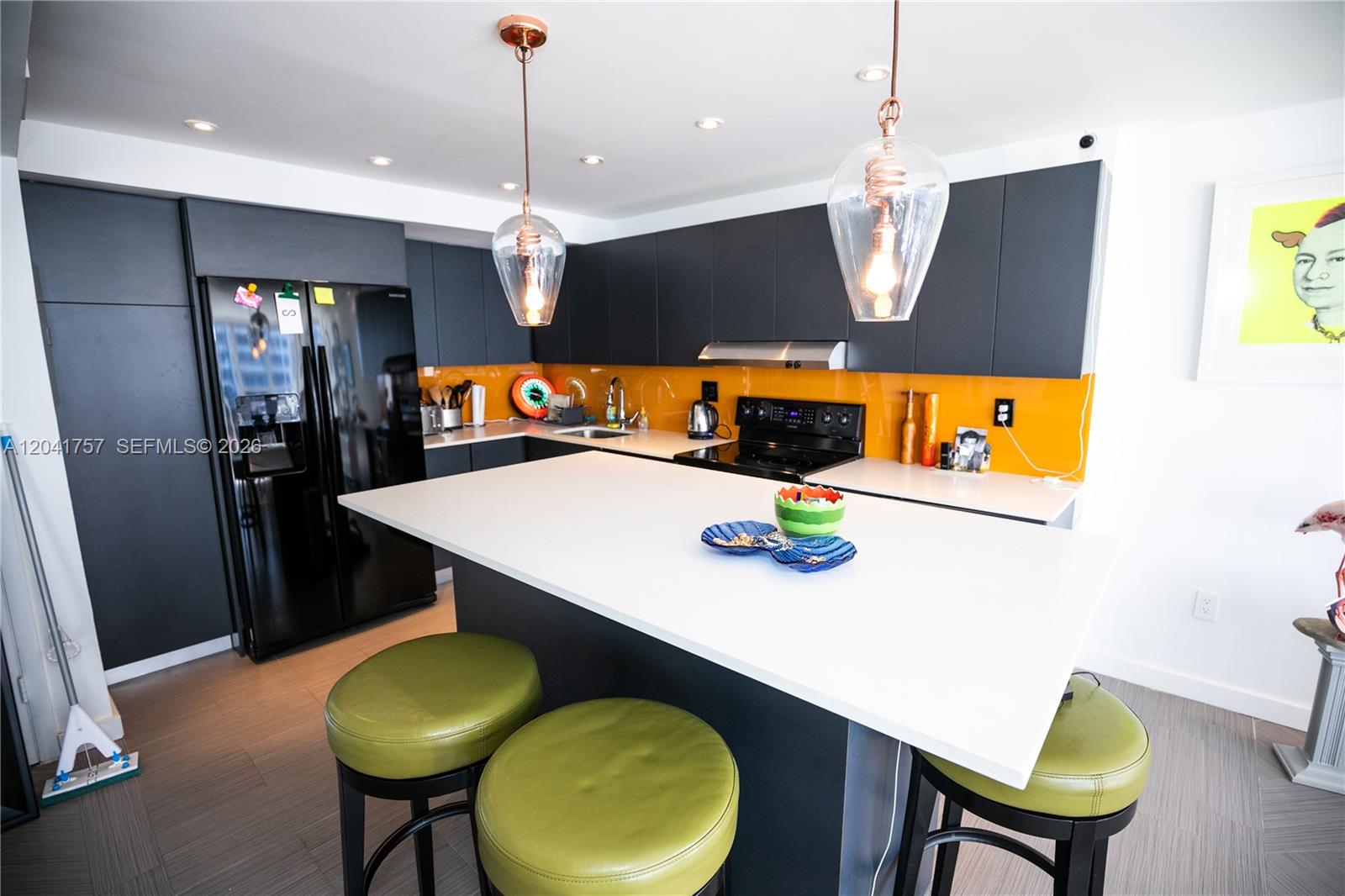 A modern kitchen features dark cabinetry, a white island, green stools, and a yellow backsplash — 600 NE 36th St, Miami FL 33137, MIAMI, FL