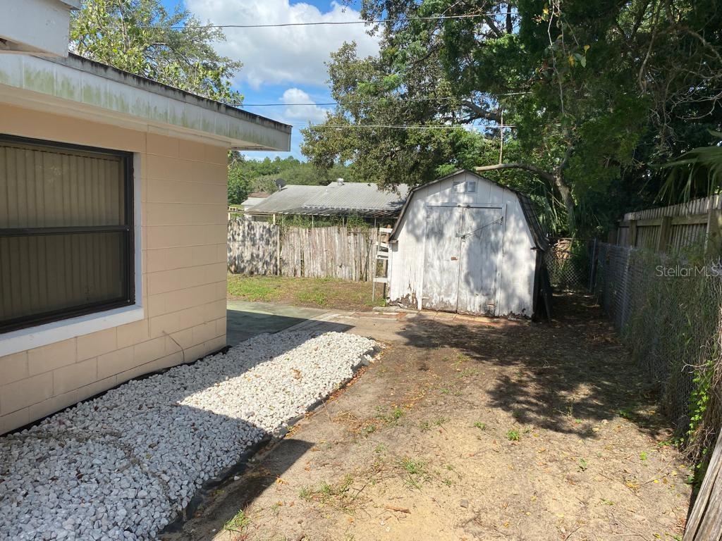 A backyard features a beige house wall, a gravel bed, and a weathered storage shed — 3408 LEEMOORE PLACE, ORLANDO, FL