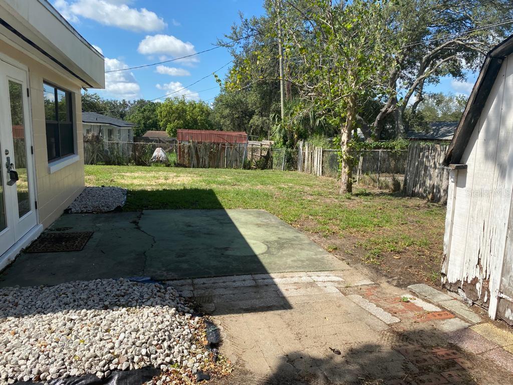A concrete patio sits in a backyard with a lawn, trees, and a wooden fence — 3408 LEEMOORE PLACE, ORLANDO, FL