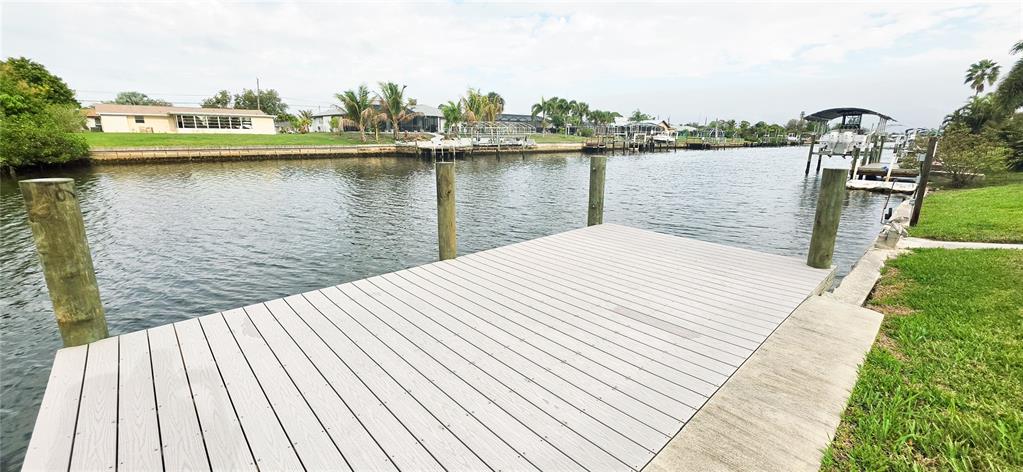 A wooden dock extends over a canal toward houses and palm trees — 392 E TARPON BOULEVARD NW, PORT CHARLOTTE, FL