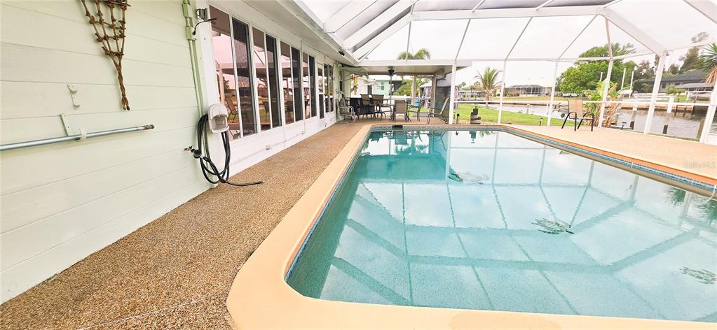 A screened-in swimming pool sits on a patio next to a light-colored house exterior — 392 E TARPON BOULEVARD NW, PORT CHARLOTTE, FL