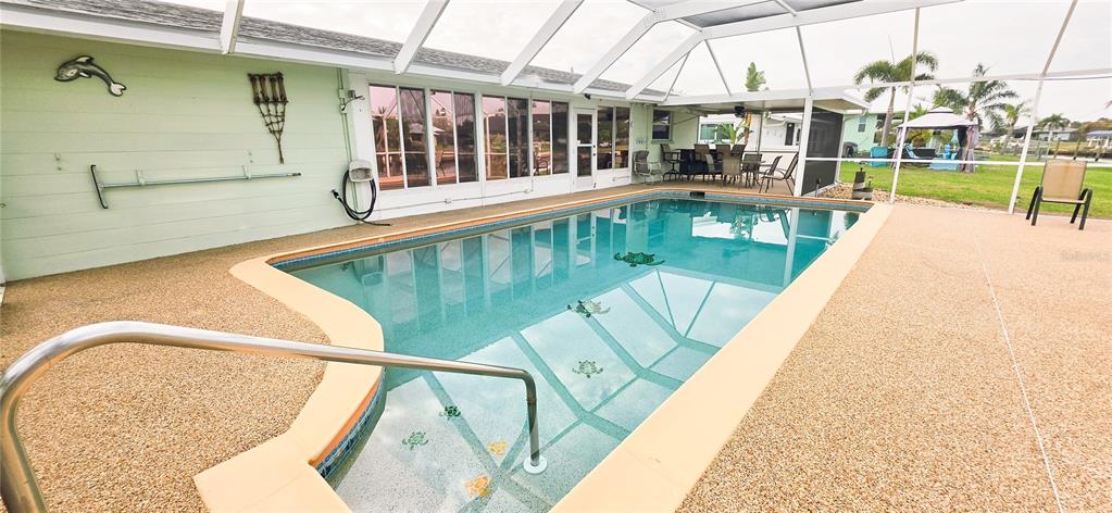 A screened-in swimming pool with a textured deck sits beside a light green house — 392 E TARPON BOULEVARD NW, PORT CHARLOTTE, FL