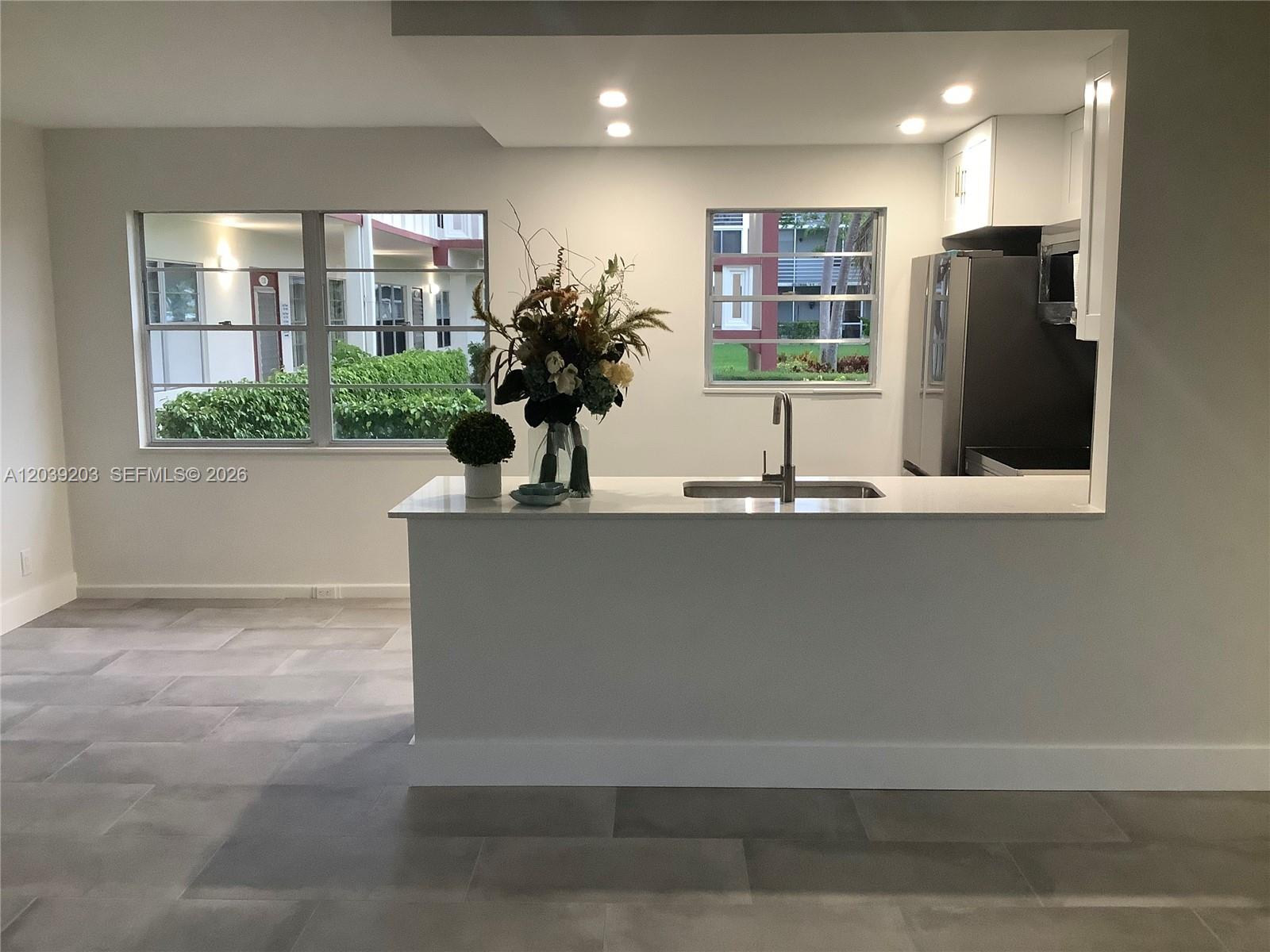 A kitchen with white cabinets, a quartz countertop island, and a sink faces two windows — 136 Brighton D # 136, Boca Raton FL 33434, BOCA RATON, FL