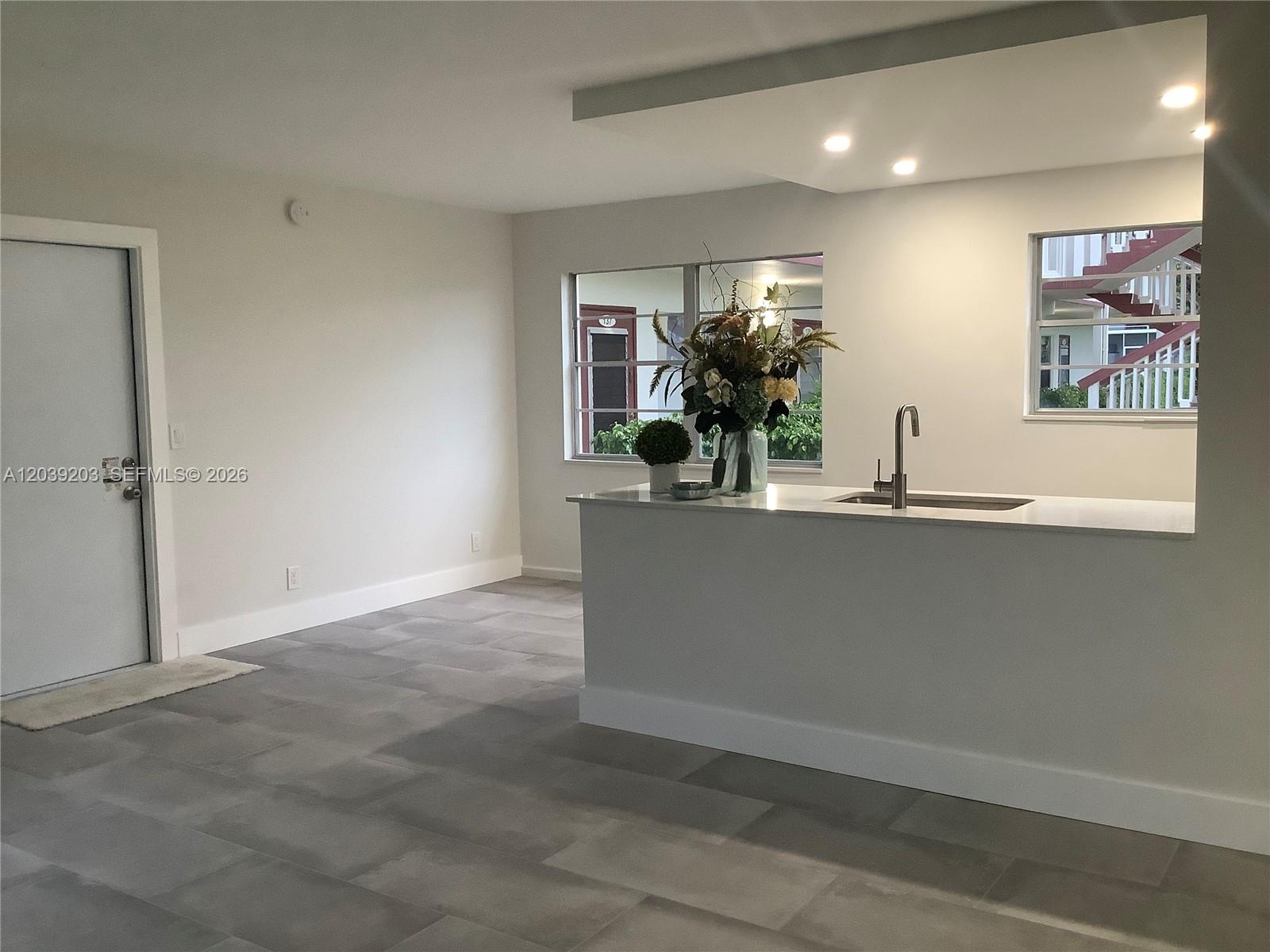 A kitchen island with a sink sits in an open-concept room with gray tile flooring — 136 Brighton D # 136, Boca Raton FL 33434, BOCA RATON, FL