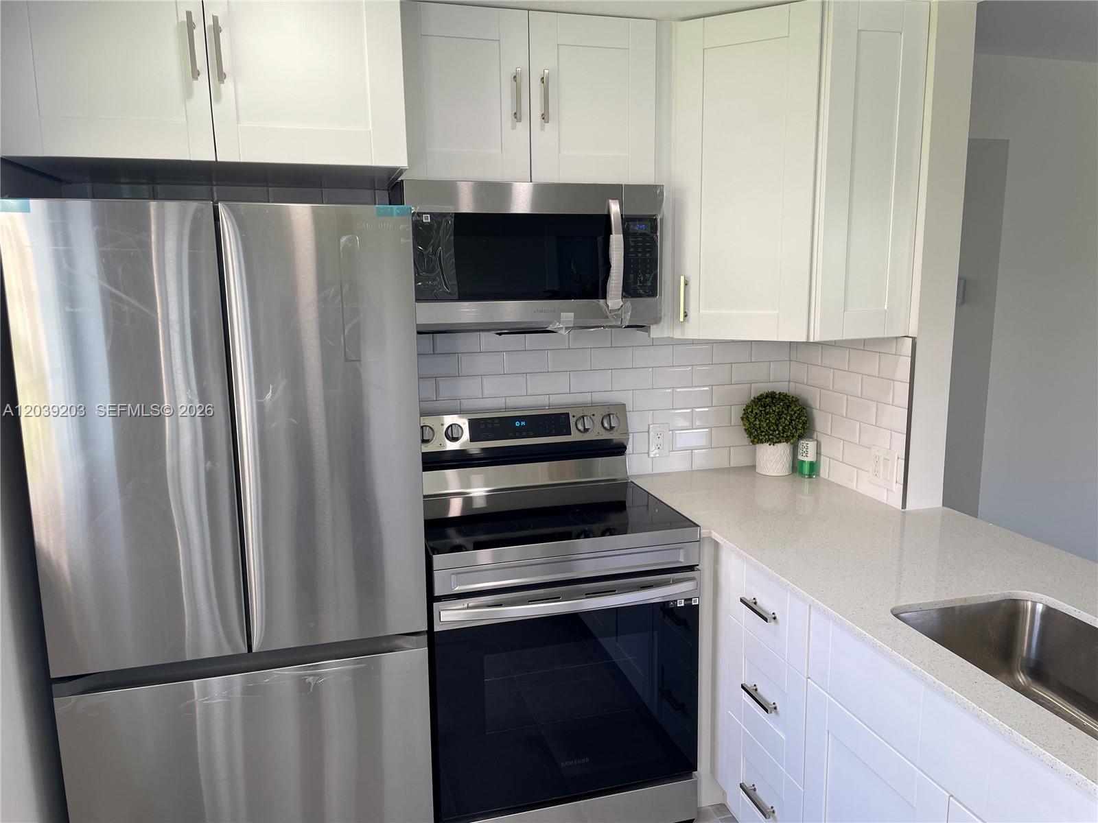 A modern kitchen features stainless steel appliances, white shaker cabinets, and a subway tile backsplash — 136 Brighton D # 136, Boca Raton FL 33434, BOCA RATON, FL
