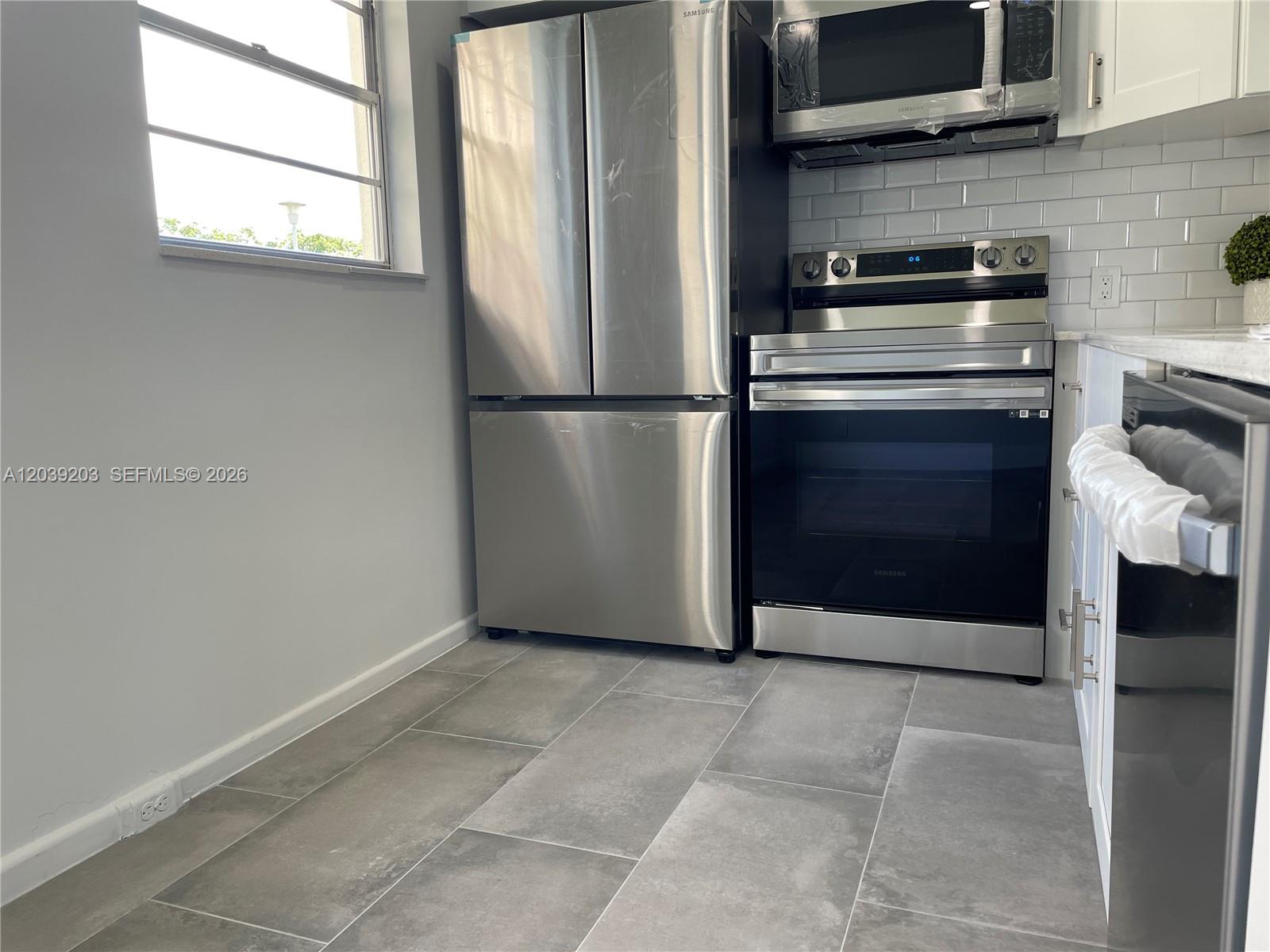 A kitchen features stainless steel appliances, white subway tile backsplash, and gray tile flooring — 136 Brighton D # 136, Boca Raton FL 33434, BOCA RATON, FL