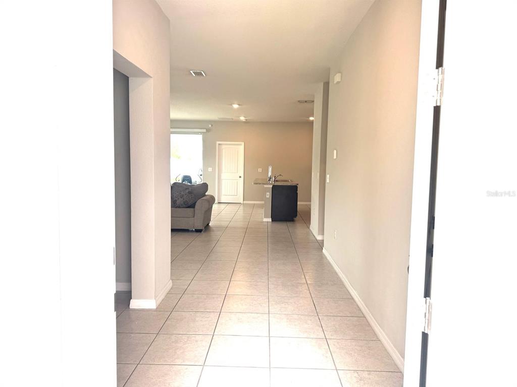 A view from an entryway looking down a tiled hallway toward an open-concept kitchen — 863 HUDSON VALLEY DRIVE, KISSIMMEE, FL