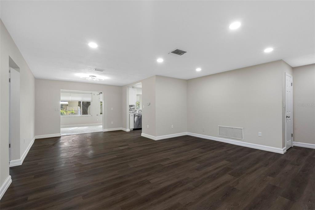 An empty room with dark wood-look flooring, recessed lighting, and a view into a kitchen — 624 ORANGE STREET, PALM HARBOR, FL