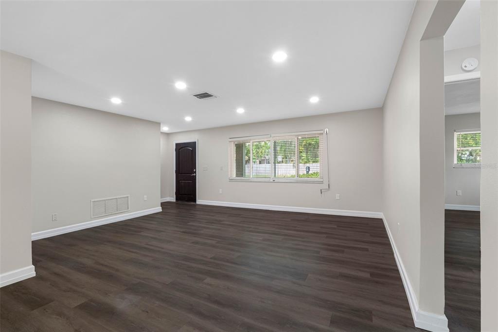 An empty living room features dark wood-look flooring, light walls, recessed lighting, and a window — 624 ORANGE STREET, PALM HARBOR, FL