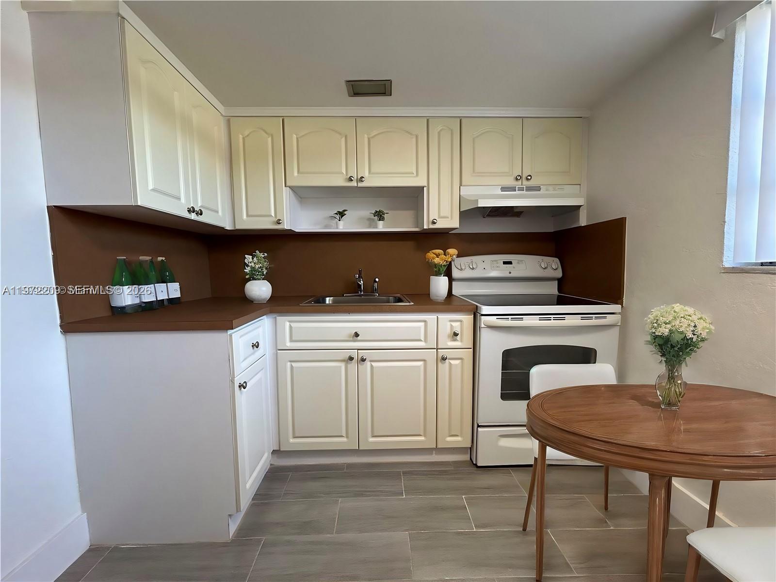A kitchen features cream cabinets, a brown backsplash, white appliances, and a small dining table — 17 NE 2nd Ave # 108, Dania Beach FL 33004, DANIA BEACH, FL