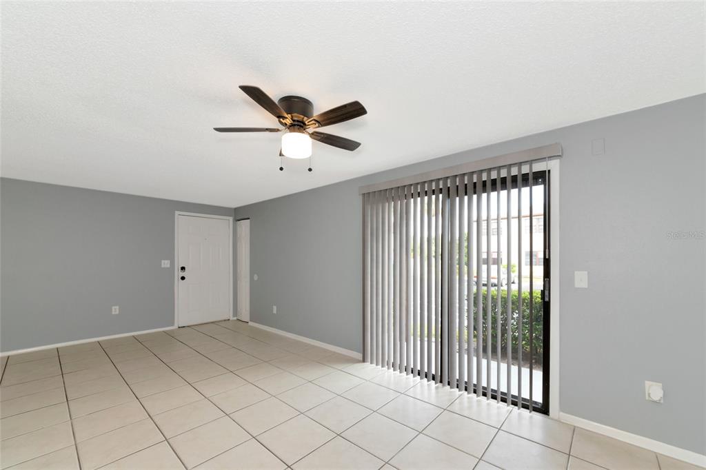 An empty room features light gray walls, white tile flooring, a ceiling fan, and sliding glass doors — 5026 WATER OAK DRIVE UNIT 109, BRADENTON, FL