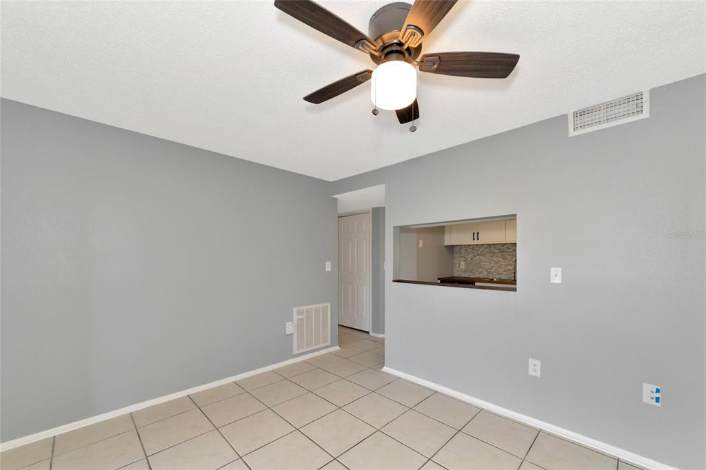 A room with light gray walls, tiled flooring, a ceiling fan, and a kitchen pass-through window — 5026 WATER OAK DRIVE UNIT 109, BRADENTON, FL