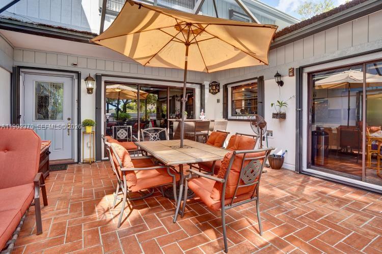 A screened-in patio features a dining set with orange cushions under a large tan umbrella — 10026 NW 52nd Ter, Doral FL 33178, DORAL, FL
