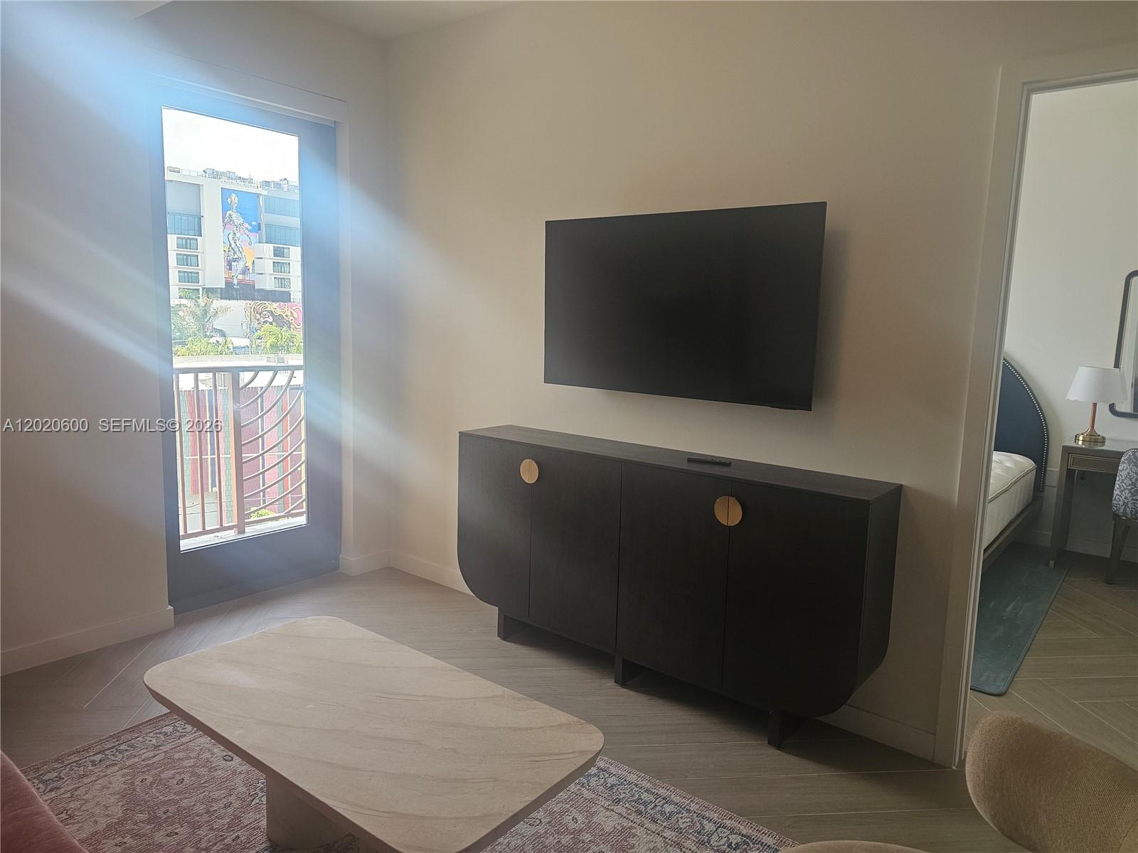 A living room features a wall-mounted television, a dark sideboard, and a balcony door — 2700 NW 2nd Ave # 312, Miami FL 33127, MIAMI, FL