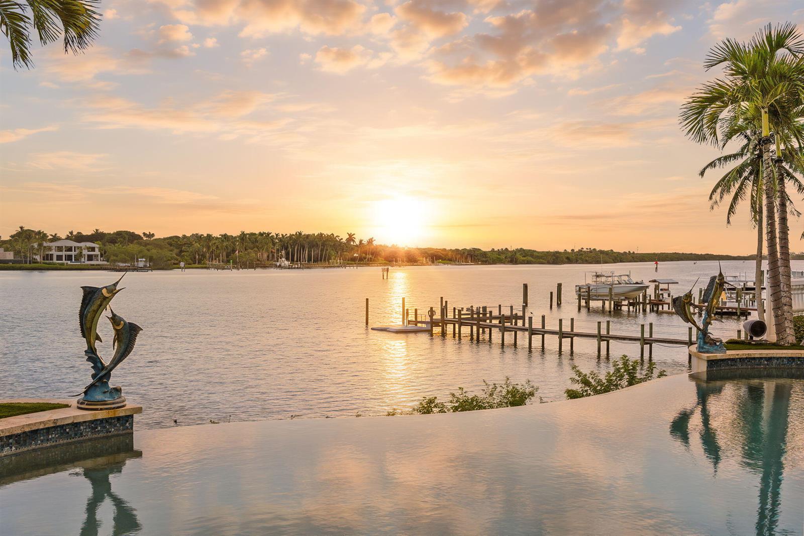 A sunset view over a waterfront infinity pool with two marlin statues and a dock — 17667 SE FEDERAL Highway, Jupiter FL 33469, JUPITER, FL
