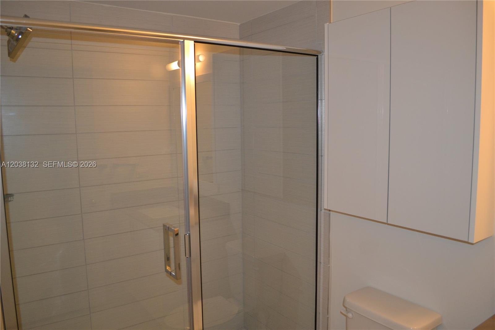 A bathroom features a glass-enclosed shower with light-colored horizontal wall tiles and white cabinetry — 999 SW 1st Ave # 3202, Miami FL 33130, MIAMI, FL