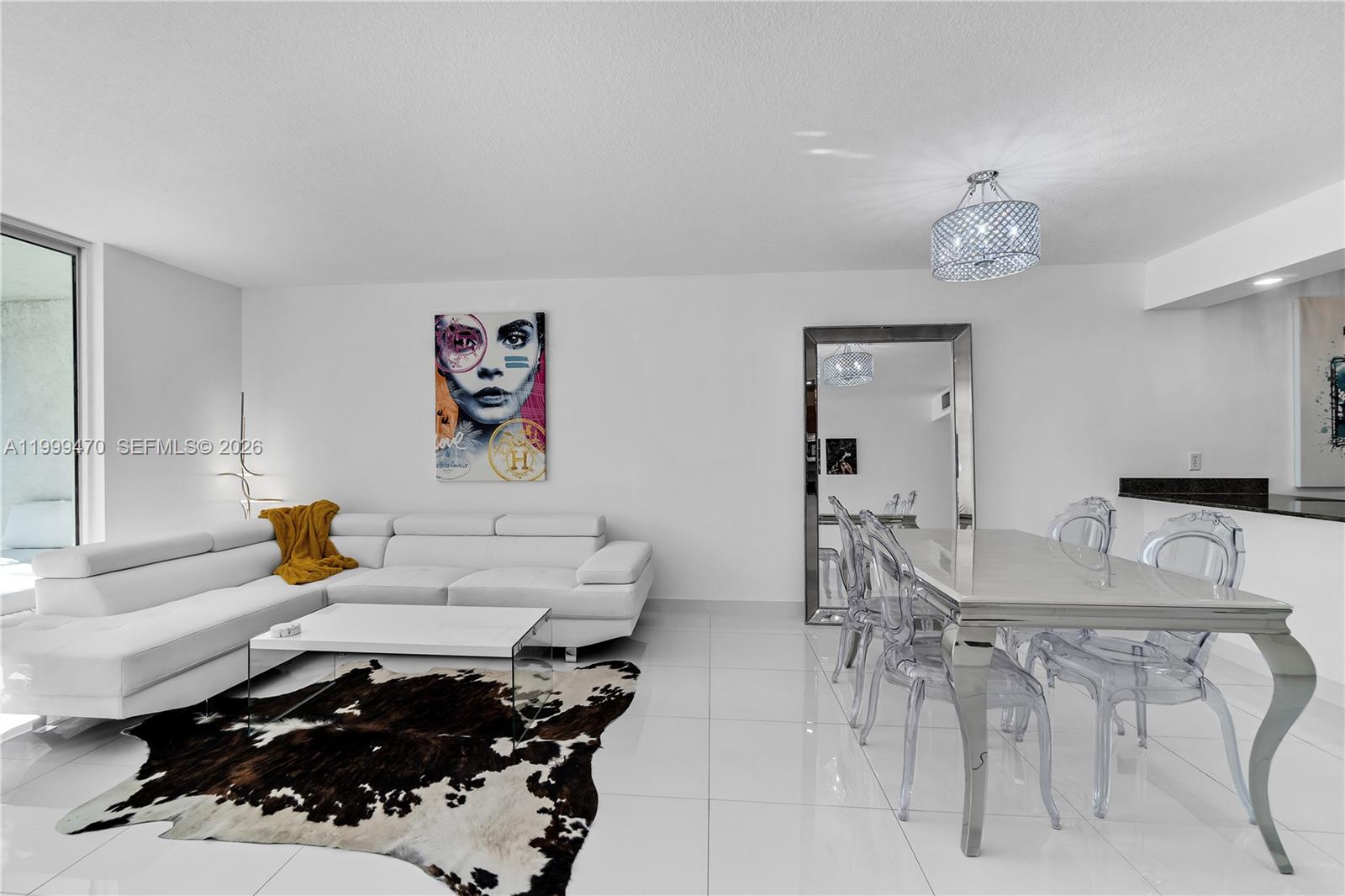 A modern living and dining area features white tile floors, a white sectional, and ghost chairs — 1200 Brickell Bay Dr # 2017, Miami FL 33131, MIAMI, FL