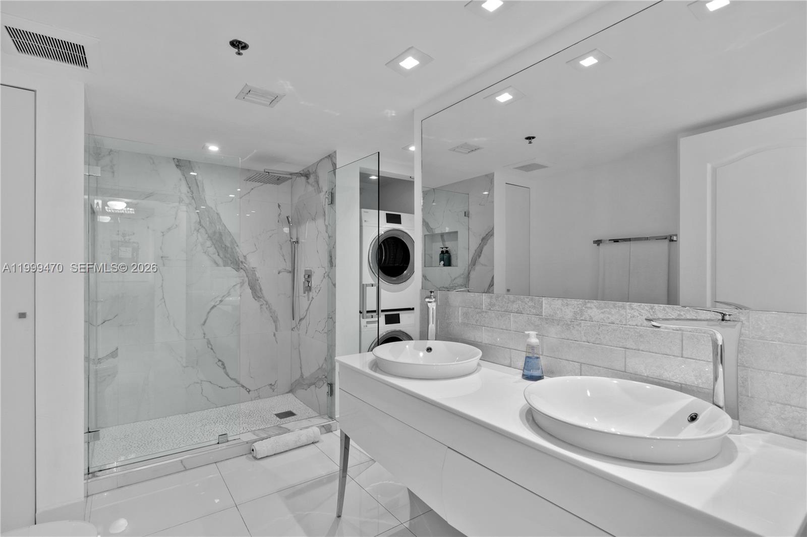 A modern bathroom features a double vanity, marble-tiled shower, and a stacked washer and dryer — 1200 Brickell Bay Dr # 2017, Miami FL 33131, MIAMI, FL