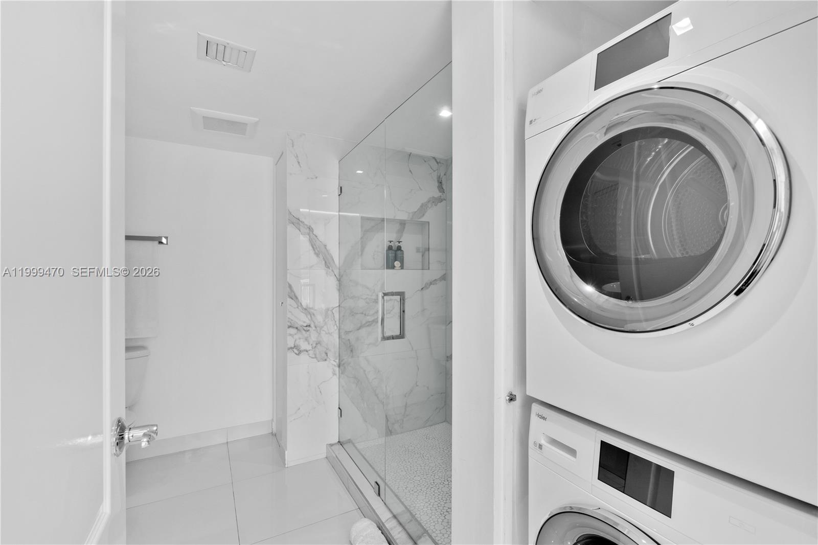 A laundry closet with a stacked washer and dryer sits beside a marble-tiled shower — 1200 Brickell Bay Dr # 2017, Miami FL 33131, MIAMI, FL