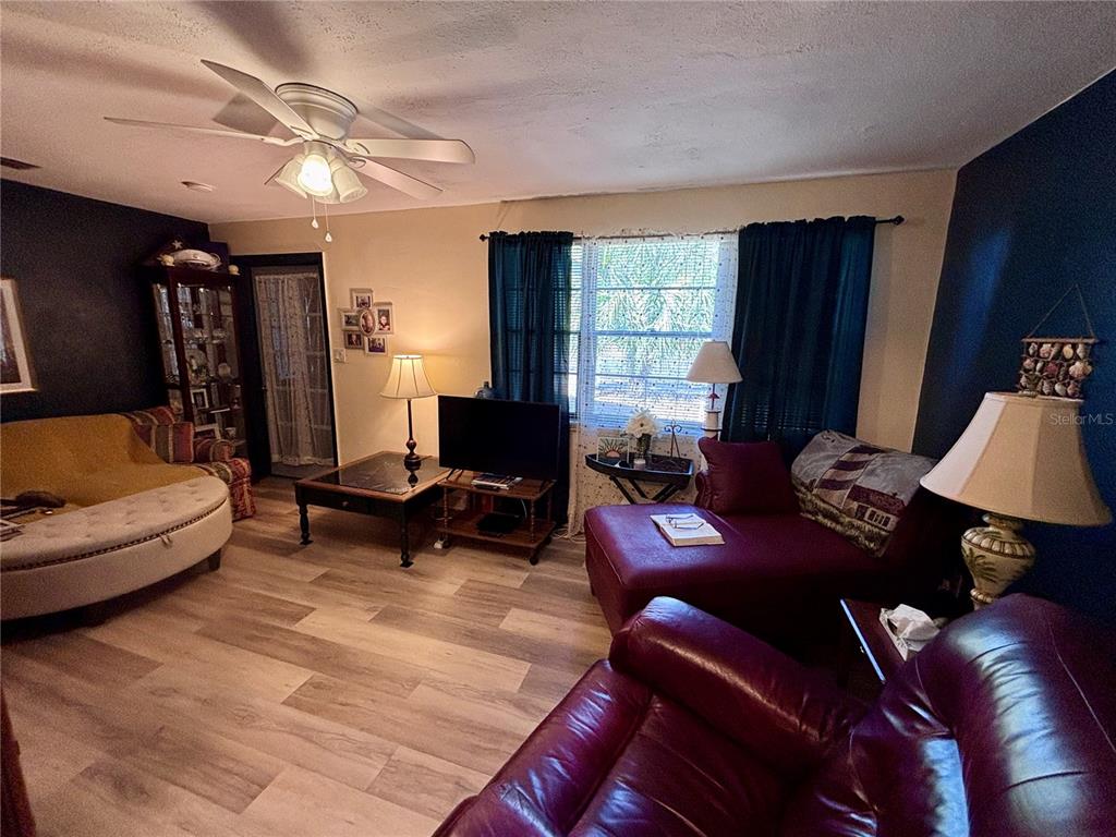 A living room features wood-look flooring, dark accent walls, a ceiling fan, and leather furniture — 3137 NW 6TH STREET, GAINESVILLE, FL