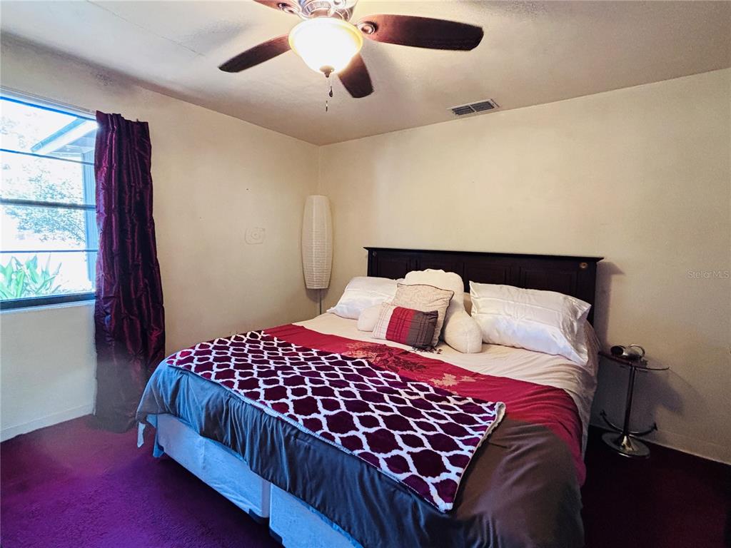 A bedroom features a bed with a patterned runner, purple carpeting, and a ceiling fan — 3137 NW 6TH STREET, GAINESVILLE, FL