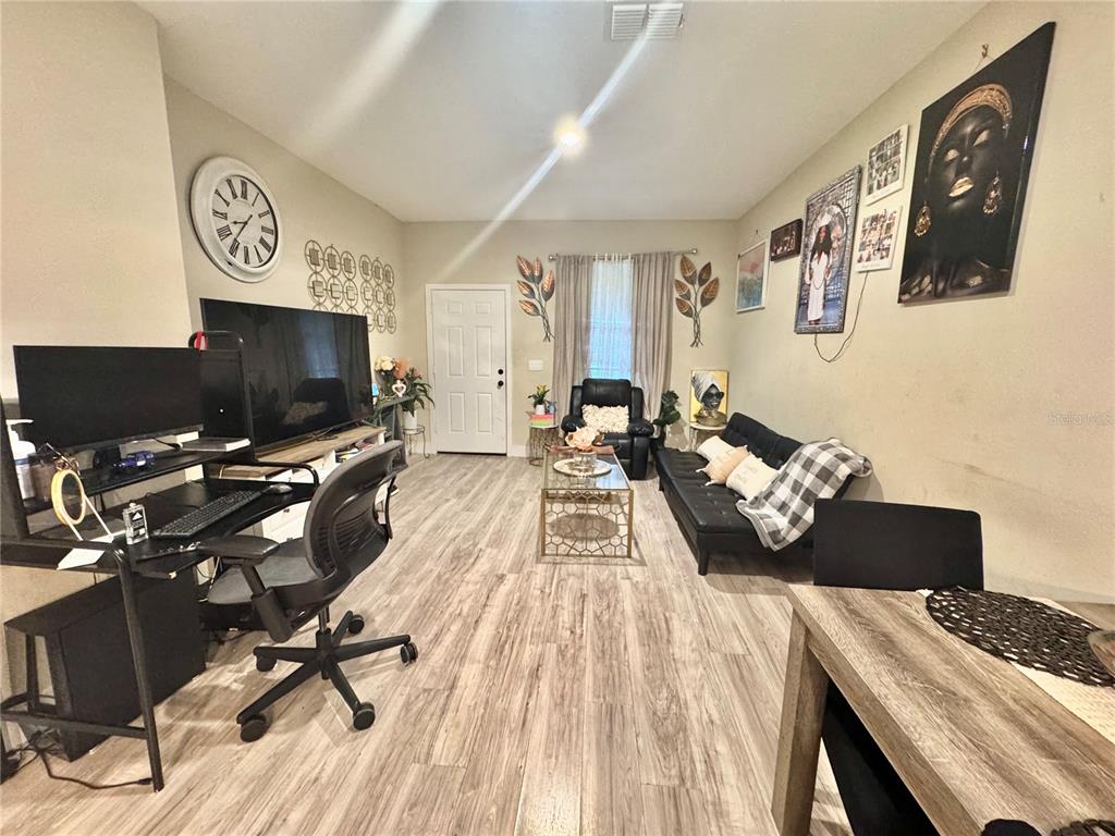 A living room features wood-look flooring, a desk, a television, and a black sofa — 113 E CLEVELAND STREET, APOPKA, FL