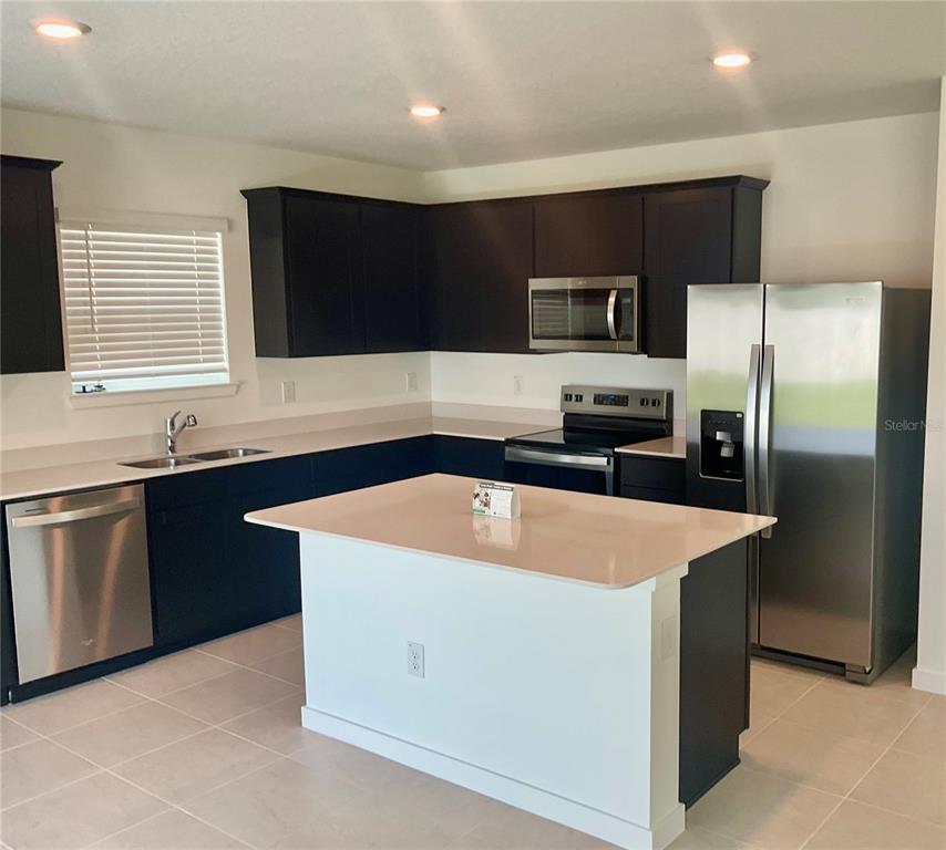 A kitchen features dark cabinets, stainless steel appliances, a center island, and light-colored countertops — 3511 HORNBEAM ROAD, SPRING HILL, FL