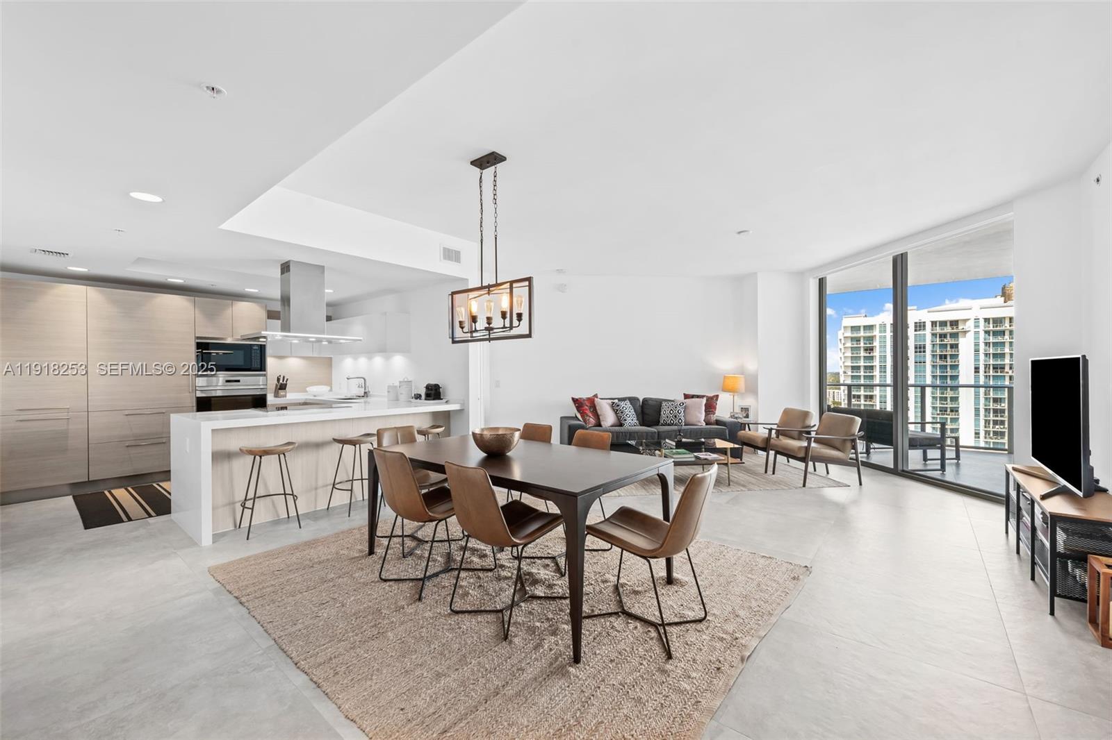 A modern open-concept living and dining area features a kitchen island, tile floors, and balcony — 17111 Biscayne Blvd # 2103, North Miami Beach FL 33160, NORTH MIAMI BEACH, FL