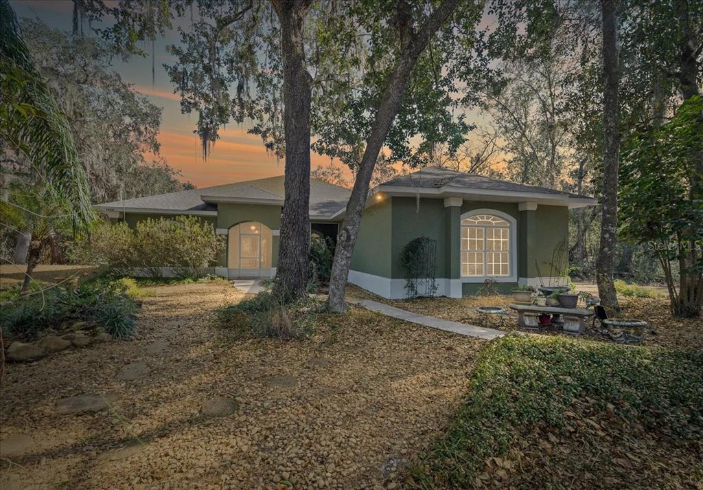 A green, single-story house with a large arched window sits in a wooded, landscaped yard — 16731 SE 181ST TERRACE, WEIRSDALE, FL