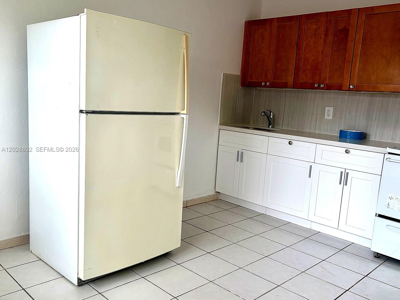 A kitchen features a light-colored refrigerator, white lower cabinets, and brown upper cabinets — 1629 Taft St # 2, Hollywood FL 33020, HOLLYWOOD, FL