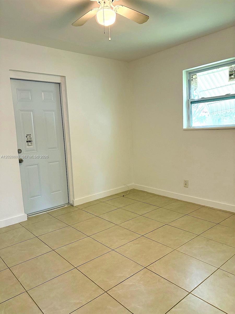 An empty room features light-colored tile flooring, white walls, a ceiling fan, and a door — 1629 Taft St # 2, Hollywood FL 33020, HOLLYWOOD, FL