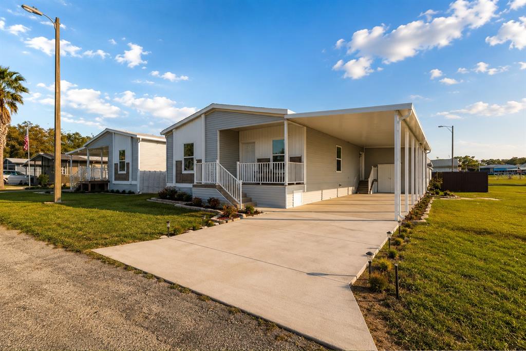 A light-colored manufactured home features a concrete driveway, a covered carport, and a front porch — 10029 HAMP DRIVE, DADE CITY, FL