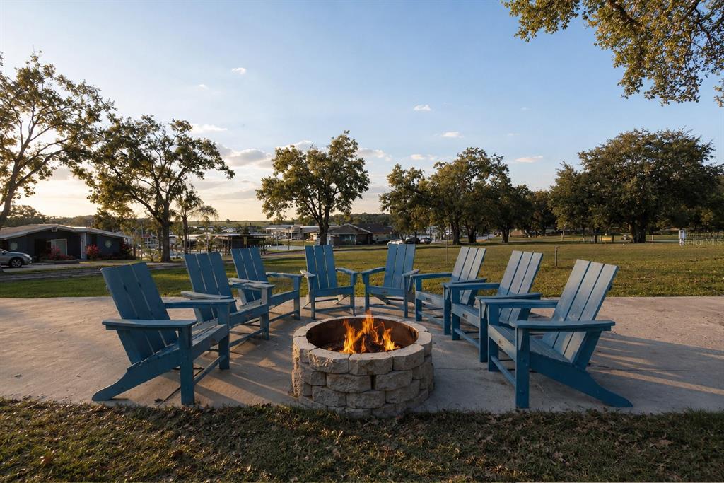 A stone fire pit surrounded by blue Adirondack chairs on a concrete patio outdoors — 10029 HAMP DRIVE, DADE CITY, FL
