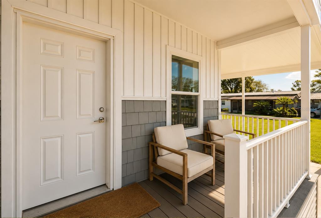 A covered porch features a white door, gray shingle siding, and two wooden patio chairs — 10029 HAMP DRIVE, DADE CITY, FL