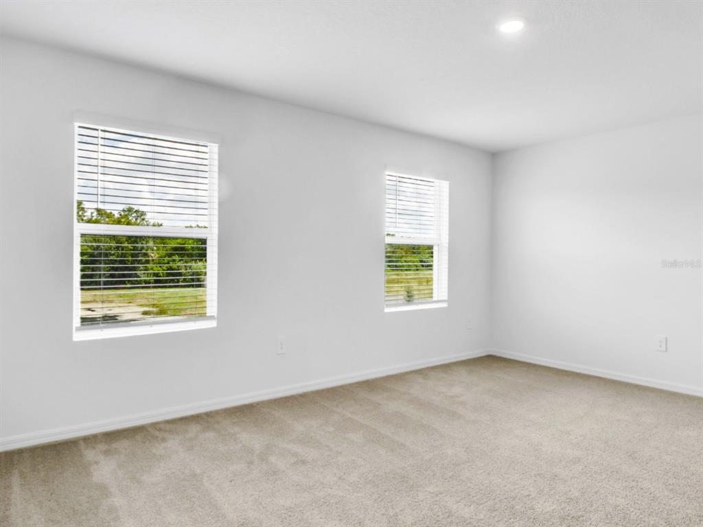An empty room features beige carpet, white walls, and two windows with blinds — 2541 SUNRAY VENUS WAY, RUSKIN, FL