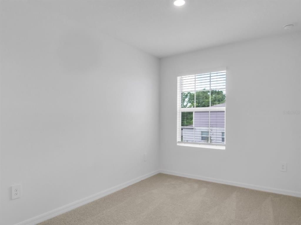 An empty bedroom features white walls, beige carpeting, and a single window with blinds — 2541 SUNRAY VENUS WAY, RUSKIN, FL