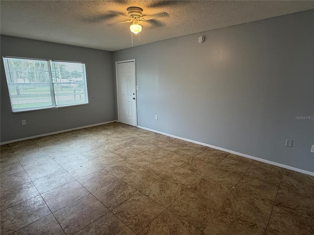 An empty room features gray walls, a ceiling fan, and brown square floor tiles — 2463 AVENUE C SW UNIT A, WINTER HAVEN, FL