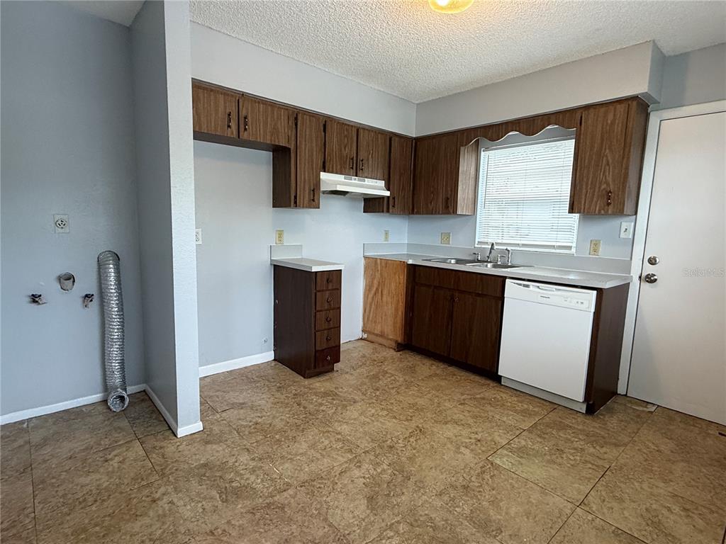 A kitchen features wood cabinets, a white dishwasher, a sink, and tile flooring — 2463 AVENUE C SW UNIT A, WINTER HAVEN, FL