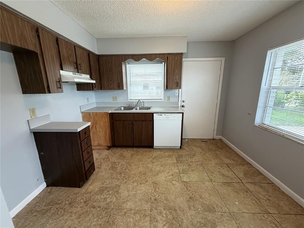 A kitchen features dark wood cabinets, a white dishwasher, and light-colored tile flooring — 2463 AVENUE C SW UNIT A, WINTER HAVEN, FL