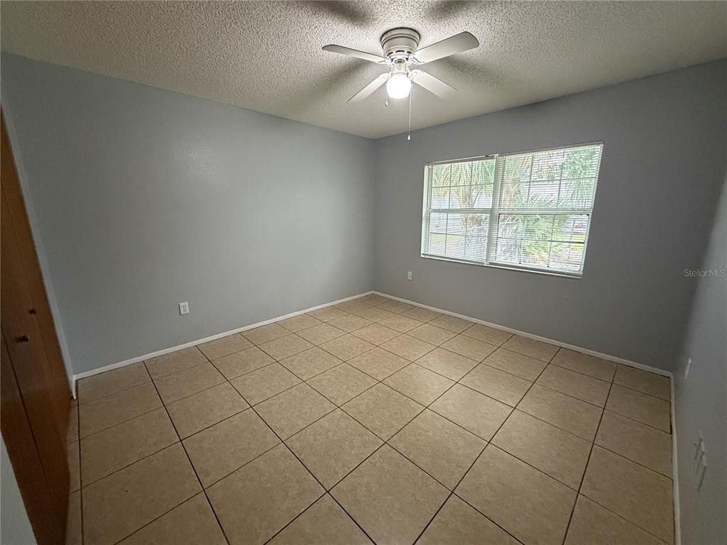 An empty bedroom features light gray walls, tan tile flooring, and a ceiling fan — 2463 AVENUE C SW UNIT A, WINTER HAVEN, FL