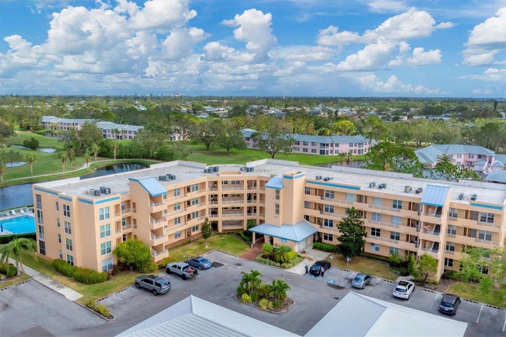 An aerial view shows a multi-story, peach-colored apartment building with a parking lot — 4530 PINEBROOK CIRCLE UNIT 208, BRADENTON, FL