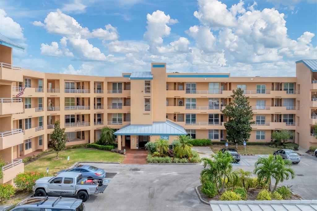 An exterior view of a multi-story, peach-colored apartment building with a central entrance and parking — 4530 PINEBROOK CIRCLE UNIT 208, BRADENTON, FL