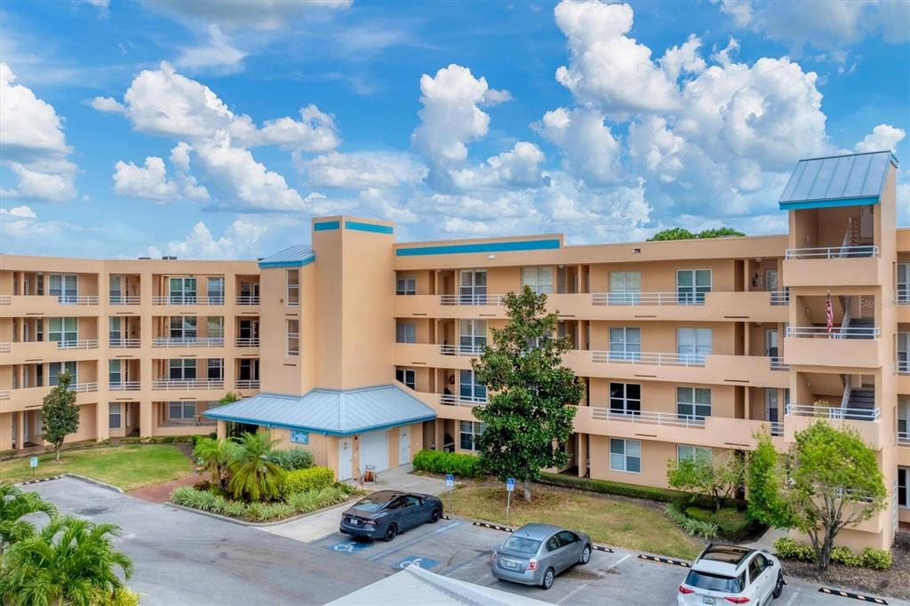 A multi-story tan apartment building with blue metal roofs and a parking lot in front — 4530 PINEBROOK CIRCLE UNIT 208, BRADENTON, FL