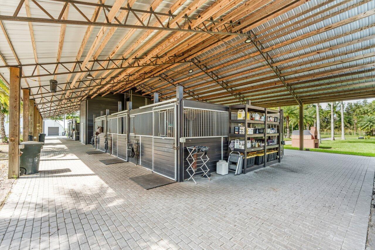An open-air horse stable with multiple stalls, a storage rack, and paved flooring — 2587 Skipiks Way, Wellington FL 33470, WELLINGTON, FL