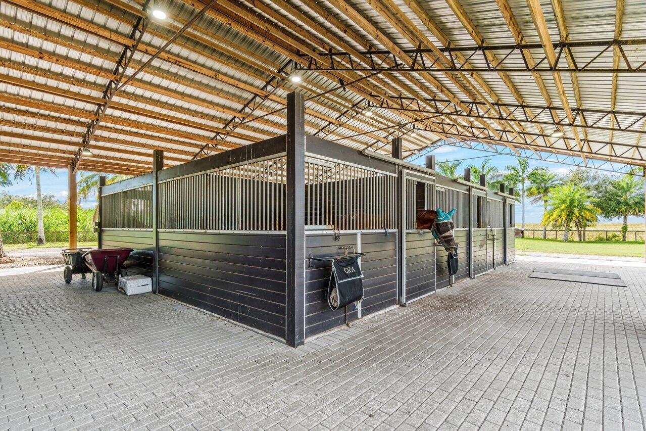 An open-air horse stable features black stalls with metal bars and a paved brick floor — 2587 Skipiks Way, Wellington FL 33470, WELLINGTON, FL